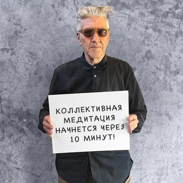 David Lynch holding a sign that says 'The collective meditation starts in 10 minutes'